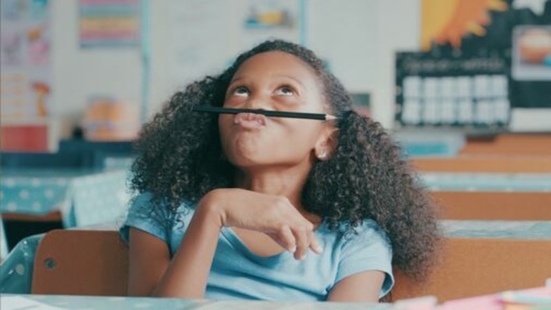 Young girl balancing a pencil on her lip distracted from work.